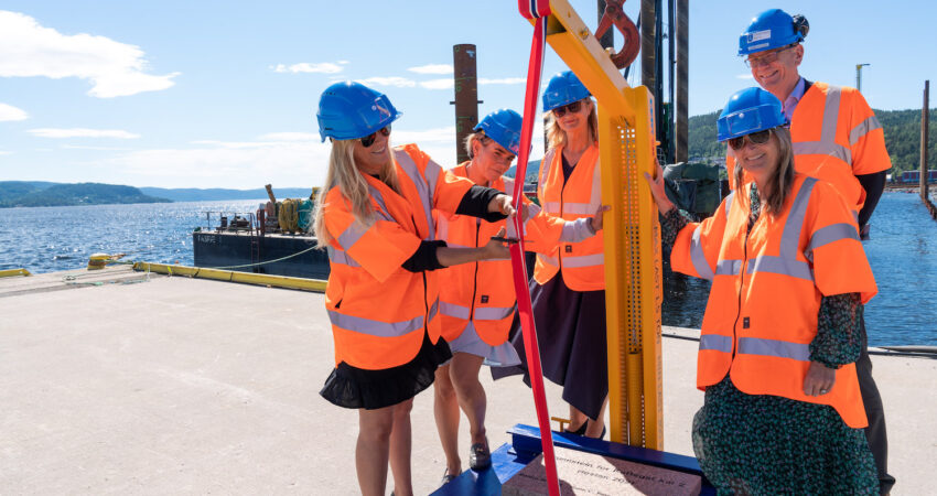 Monica Berg klipper snor i flaggets farger som henger paa en kran. Cecilie Ringdal, Ann-Christin Andersen, Arne Fosen og Lene Conradi staar rundt i orange vester og blaa hjelmer